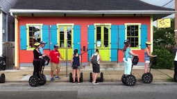 A group of people stand on Segway's outside a colourful house in New Orleans.