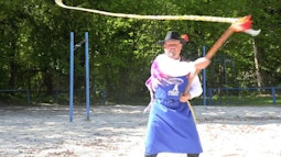 A person stands in a sandy park cracking a large whip.