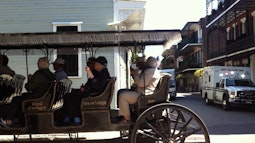 A group of people ride a large wooden cart through a New Orleans street.