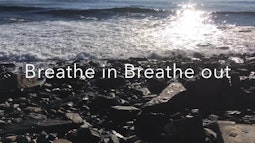 In low sunlight a small waves breaks on rocks. Over the top is the text 'Breathe in Breathe out'.