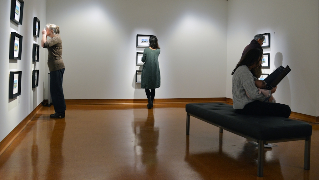People in a gallery looking at framed artworks on the wall