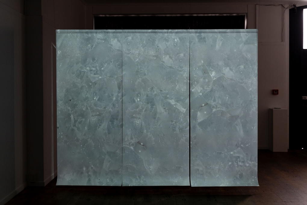 Installation view of a darkened gallery space. A large screen projects a close-up image of geometric patterns in ice.