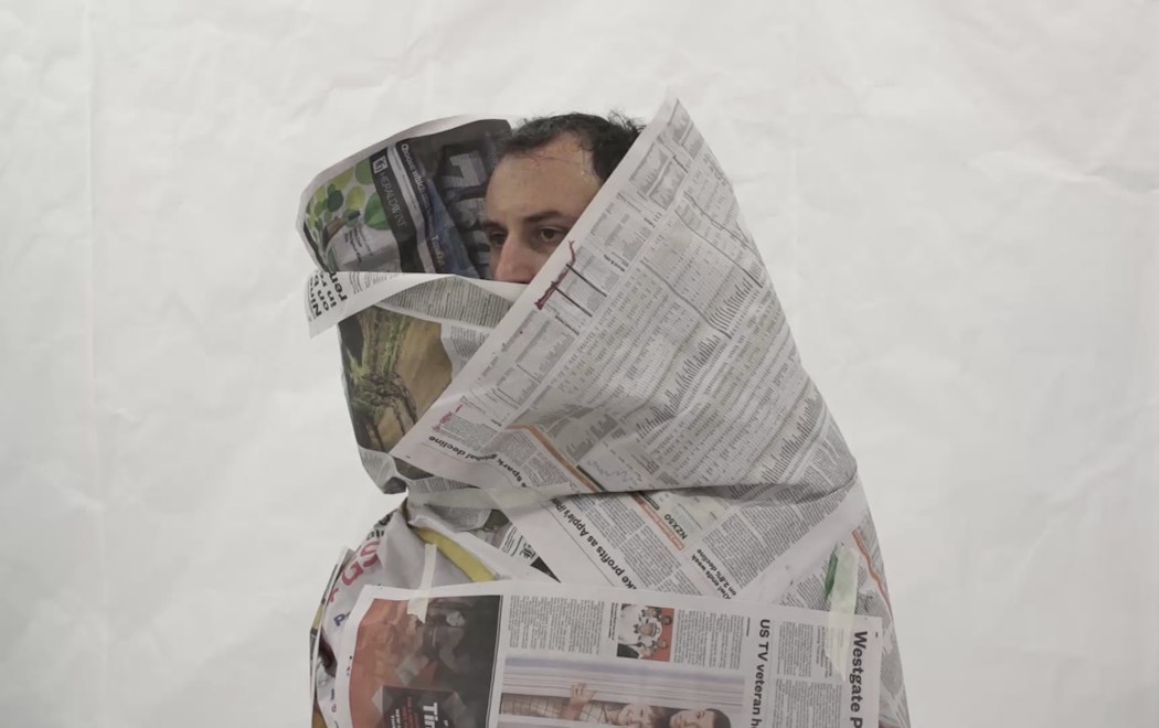 A man peers out from a costume made of newspapers