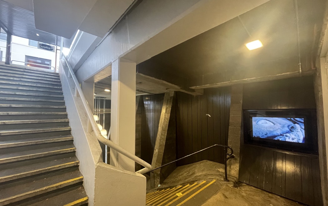 A stairwell with the Masons Screen public art video monitor displaying an image of a rock form by Phil Dadson
