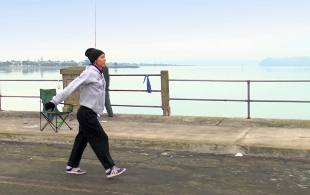 A person in a tracksuit and beanie dances along a bridge.