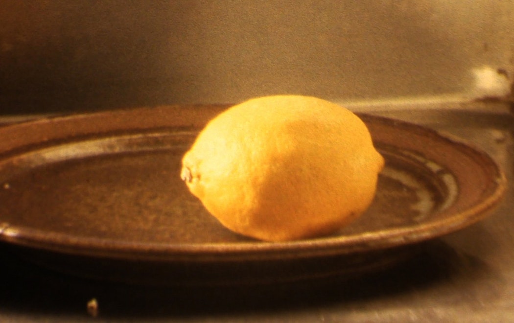 A single lemon sits on a brown ceramic plate with soft daylight