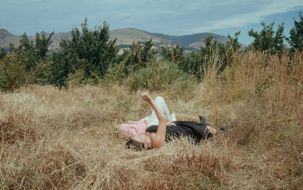 Two women lie in dry grass in hills and look up at the sky