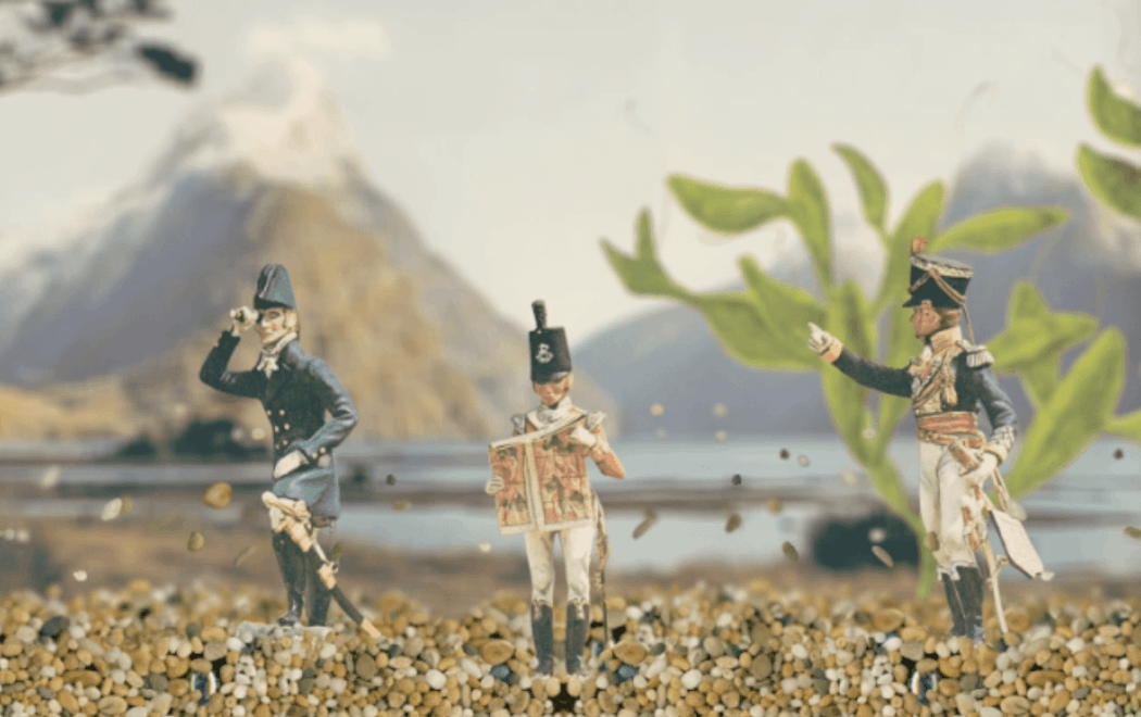 Three military model figures are standing in the stony bottom of a fish tank. A landscape is suggested by a picture of a mountain in the background, and green oxygen weed in the mid-ground.