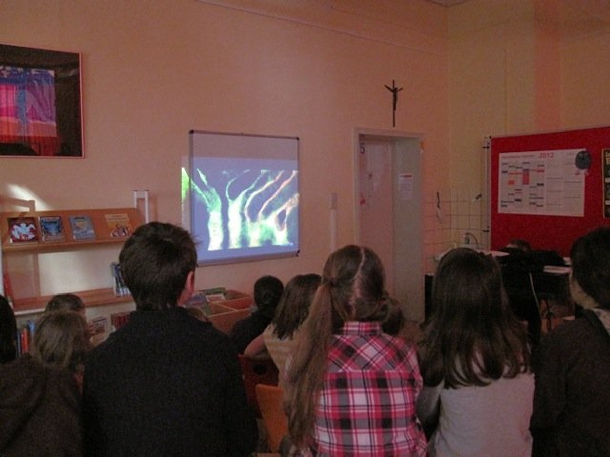 A group of children watches a video projected onto a wall in a classroom