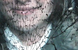 A person smiles behind a screen of cracked glass.
