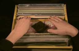 A pair of hands flick through a box of records.