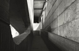 A brutalist concrete walkway, light comes in from windows in the distance.