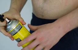 A topless person opens a can of expanding foam.