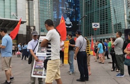 In a public square a group of people meet and talk, some are holding the Chinese flag.