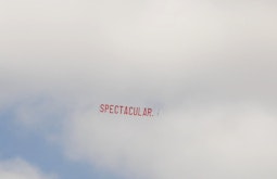 A large banner reading Spectacular flies behind a plane on a cloudy day.