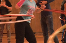 In a gymnasium a group of people practice using hula hoops.