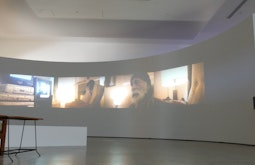 A large semi-circular wall in a gallery with videos projected on it.
