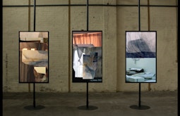 Three tv monitors are mounted portrait on metal beams with video collages playing.