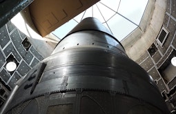 A large shiny metal rocket in a construction bay with a glass ceiling.