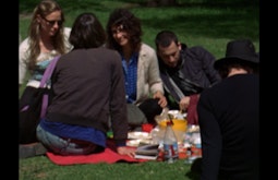 A group of people sit on a blanket having a picnic on a sunny day.