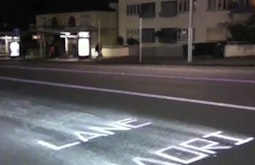 On a suburban street the words Maori Lane have been painted onto the road in the style of road markings.