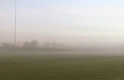 On a rugby field a figure runs through thick fog as the sun rises.