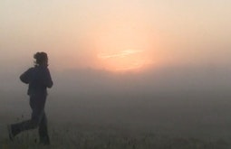 A person runs towards through thick fog towards a sunrise.