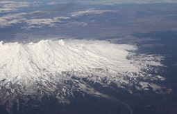 A snowy mountain and the surrounding environment is seen from a plane.
