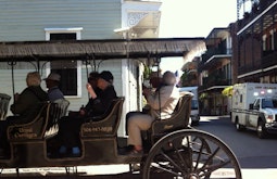 A group of people ride a large wooden cart through a New Orleans street.