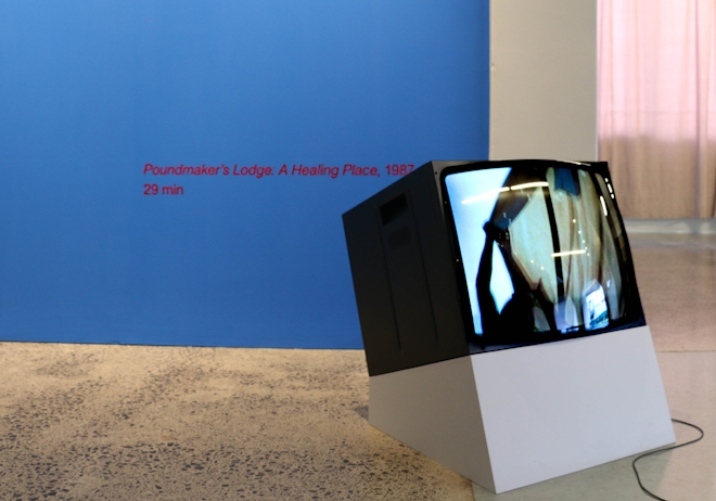 A TV monitor sits on a plinth in a gallery space.