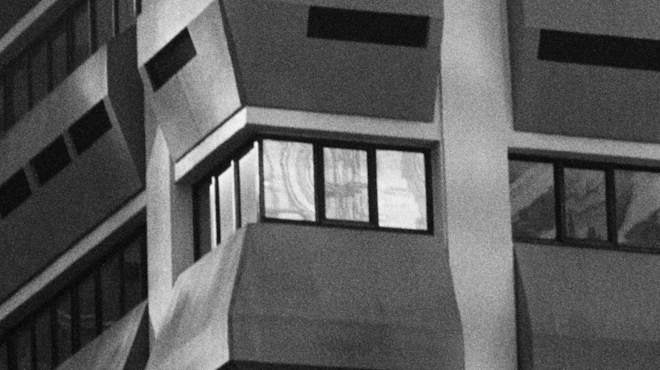 A black and white film still of reflections in the windows of a high-rise building