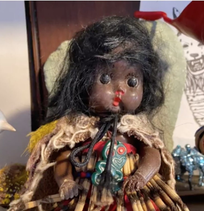A worn tourist souvenir doll which is dressed and adorned to represent a Māori girl