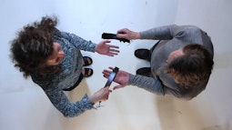 A birds-eye view of two people as they stand using straps to slap each-others open palms.