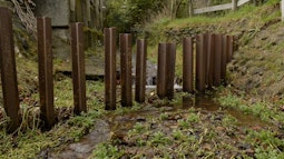 Metal stakes make a fence through a small stream.