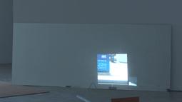 A film of a street is projected on a white wall.