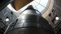 A large shiny metal rocket in a construction bay with a glass ceiling.