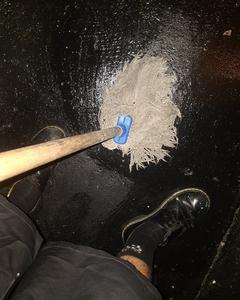 A hairy mop is being pushed against a shiny black concrete floor in a sex on site club. The image is taken looking down at the mop and the artists feet probably mid way through mopping the floor.