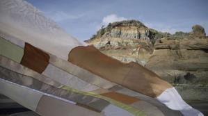 A delicate patchwork fabric of slight translucency is dancing in the wind in front of a rocky landscape.