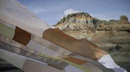 A delicate patchwork fabric of slight translucency is dancing in the wind in front of a rocky landscape.