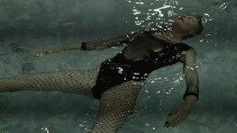 A person wearing tights and swimming costume lies on their back in a pool, eyes closed