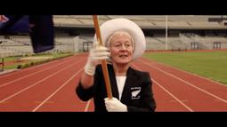 A person wearing a white hat and gloves walks along a running track in a stadium. They are carrying a flag pole.
