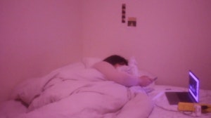 A person lies in bed while using their phone and laptop, the room is all pink.