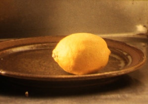 A single lemon sits on a brown ceramic plate with soft daylight