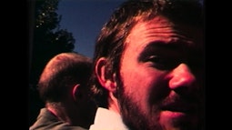 A person looks over their shoulder towards the camera, their face is red in the sun.