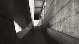 A brutalist concrete walkway, light comes in from windows in the distance.