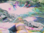 Multiple images of people playing in and laying next to a stream are overlaid in layers of cyan magenta yellow and black.