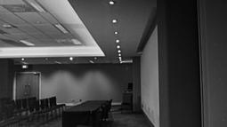 A black and white scene shows rows of empty chairs face a large table in an empty conference room.