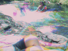 People play near a river or waterfall, laying near the water or swimming. The image has been made with a photographic technique called three colour separation, in which the scene is filmed three times, and each negative given a red, blue and green primary colour. These negatives are layered on top of each other, and combined into one image, which appears to show an ‘after-image’ of different movements recorded in each shot.