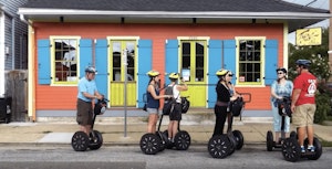 A small tour group of people on electric segways are assembled in front of a brightly coloured cafe in the Tremé district of New Orleans.