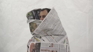 A man peers out from a costume made of newspapers